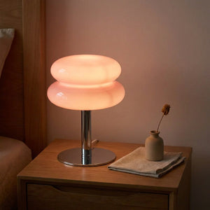 Lampe de chevet en verre forme macaron rose allumée sur une table de nuit