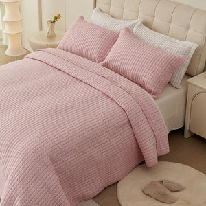 Couvre-lit matelassé rose à fines lignes matelassées installé sur un lit fait
