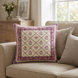 Housse de coussin carrée ivoire à treillis floral rose et bordure violette sur un canapé beige