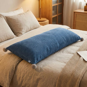 Coussin long en velours côtelé bleu orné de pompons sur un lit