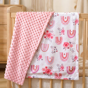 Couverture bébé minky réversible rose à motif arc-en-ciel pliée sur un lit à barreaux