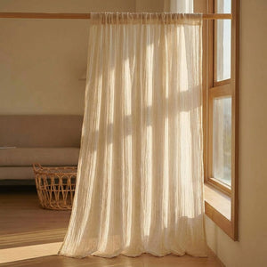 Rideau voilage beige aspect lin suspendu devant une fenêtre en bois avec panier en osier