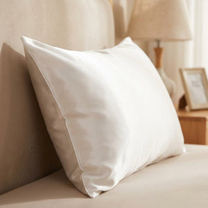 Taie d'oreiller satin blanche posée sur un lit contre une tête de lit