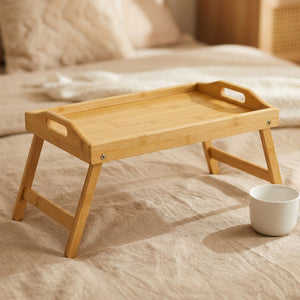 Plateau bambou couleur naturel avec pieds pliables déployés sur lit en lin beige