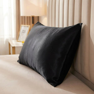 Taie d'oreiller satin noire posée sur un lit contre une tête de lit