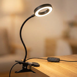 Lampe pince noire à col de cygne allumée clipsée sur un bureau