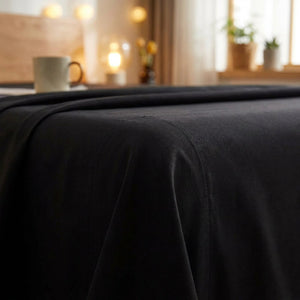 Drap plat en coton noir replié sur un lit dans une chambre chaleureuse