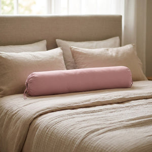 Traversin cylindrique rose posé sur un lit contre une tête de lit