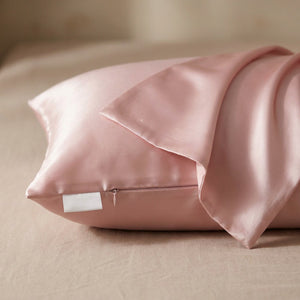 Taie d'oreiller en soie rose posée sur un tissu de lin beige