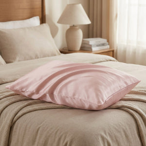 Taie d'oreiller en soie rose posée sur un lit avec couverture beige