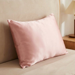 Taie d'oreiller satin rose posée sur un lit contre une tête de lit