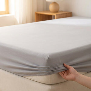 Drap housse gris clair installé sur un lit avec bande élastique visible