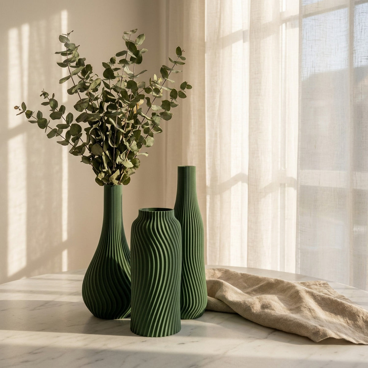 Lot de 3 vases côtelés verts sur surface marbre avec eucalyptus et voilage
