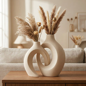 Duo de vases en céramique beige enlacés garnis de pampas posés sur une table en bois