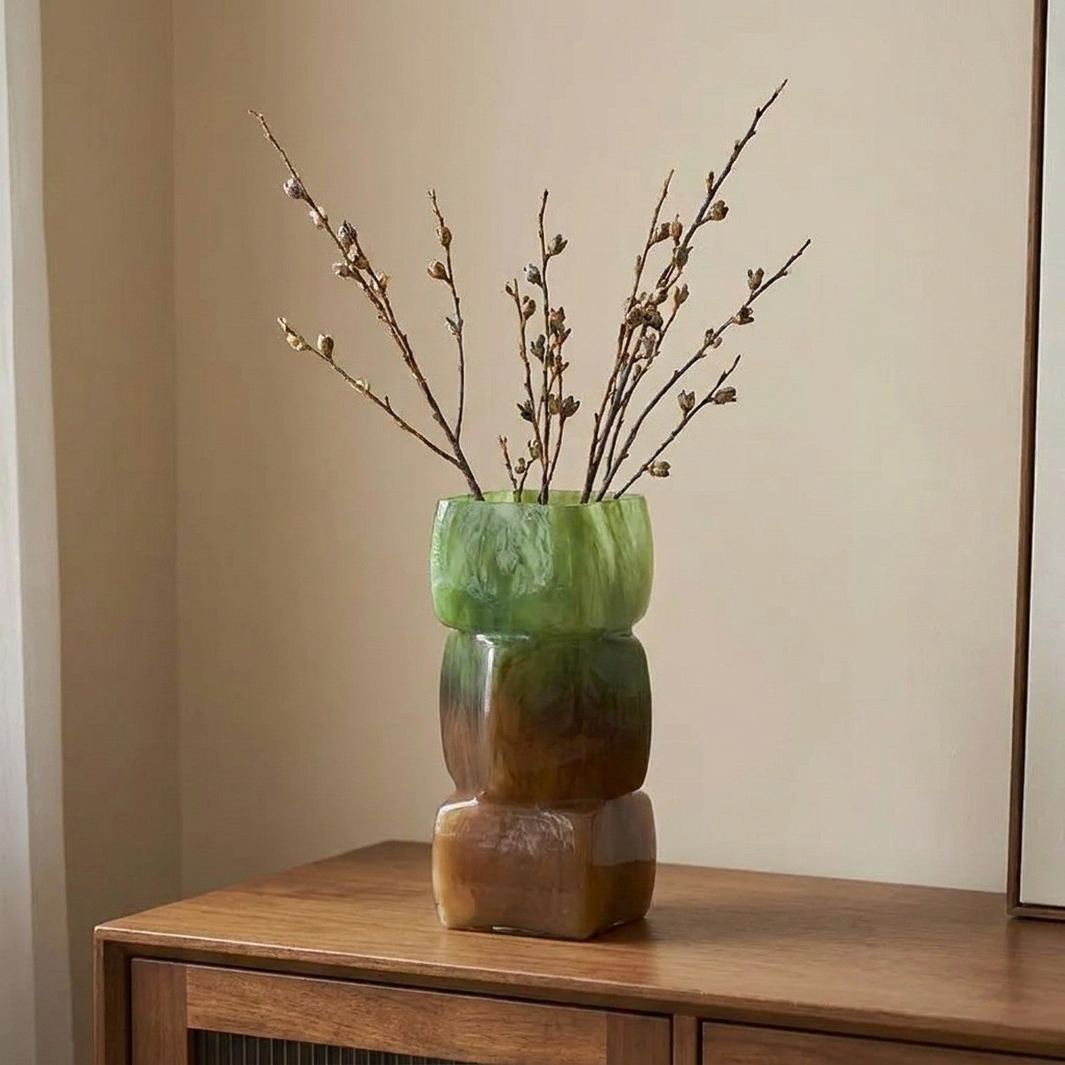 Vase géométrique vert et ambré avec branches sur une enfilade en bois