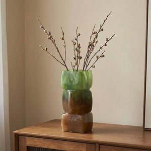 Vase géométrique vert et ambré avec branches sur une enfilade en bois