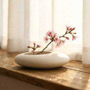 Vase galet blanc sur un rebord de fenêtre avec une branche de fleurs roses