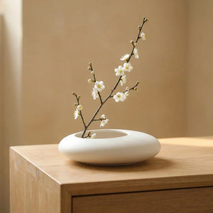 Vase galet en céramique blanche avec une branche de fleurs blanches posé sur une console en bois