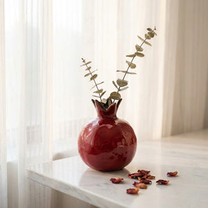Vase grenade en céramique rouge sur une surface en marbre avec eucalyptus