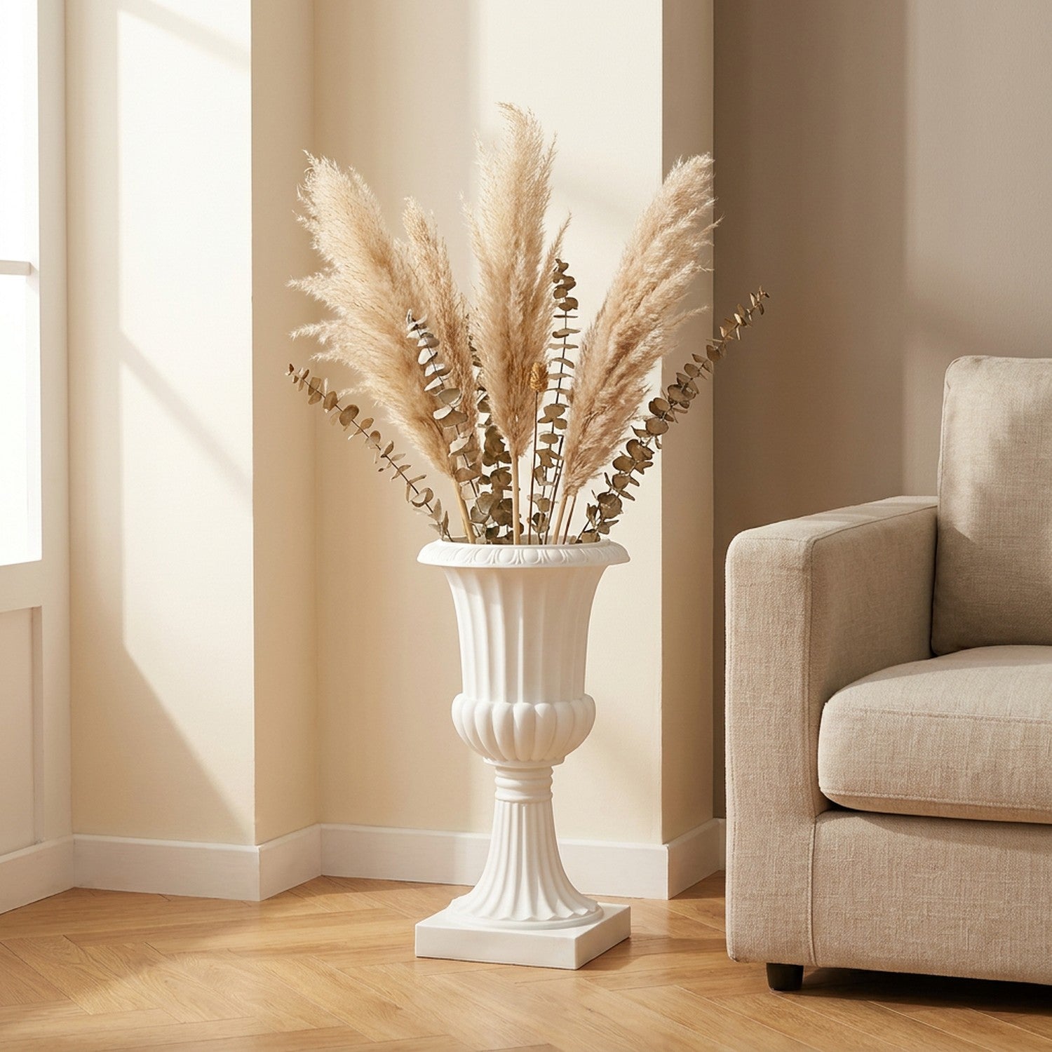 Vase médicis blanc avec herbes de pampa et eucalyptus dans un salon moderne près d'un fauteuil beige