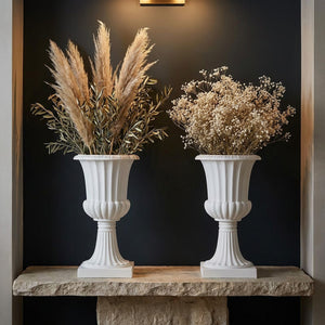 Deux vases médicis blancs posés symétriquement sur une console en pierre devant un mur sombre