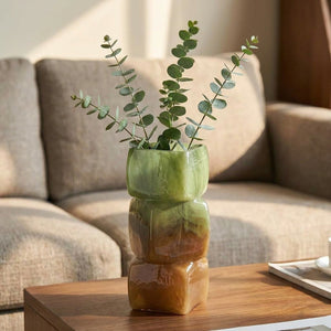 Vase géométrique vert et ambré avec eucalyptus sur une table de salon