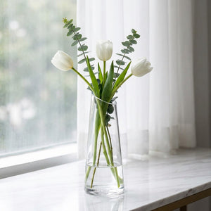 Vase en verre transparent bouche inclinée avec fleurs blanches sur marbre