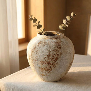 Vase en céramique wabi sabi rond avec eucalyptus séché près d'une fenêtre