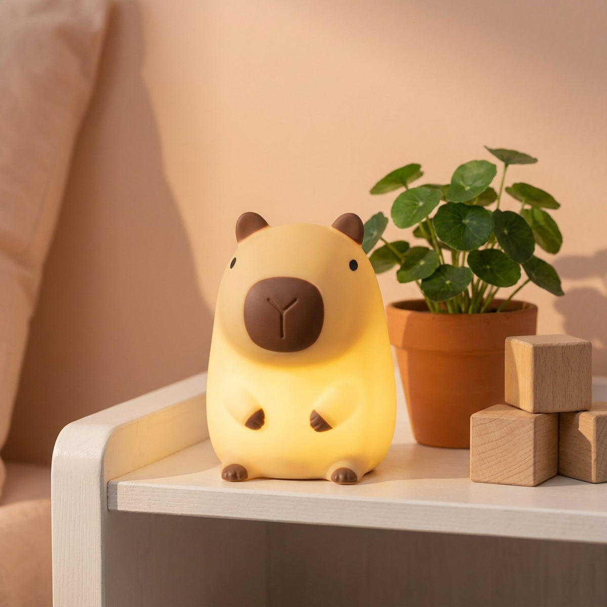 Veilleuse capybara allumée sur une étagère blanche avec plante verte et cubes en bois
