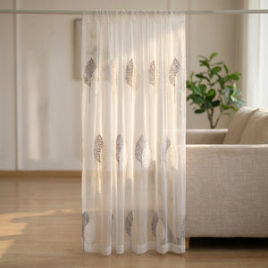 Voilage en tulle blanc au motif d'arbres brodé suspendu à une fenêtre lumineuse d'un salon