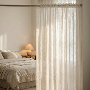 Voilage blanc suspendu à la fenêtre d'une chambre cocooning en lumière douce