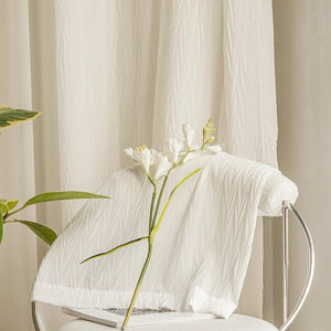 Tissu plissé blanc drapé sur une chaise devant un voilage suspendu et une fleur