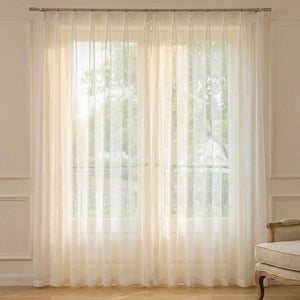 Voilage en tulle blanc à texture chevron suspendu devant une fenêtre lumineuse dans un intérieur chaleureux