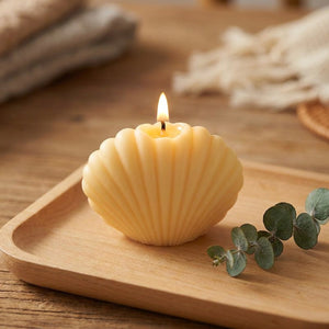 Bougie coquillage jaune pastel allumée sur un plateau en bois avec de l'eucalyptus