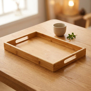 Plateau de service rectangulaire en bambou clair avec poignées découpées posé sur une table en bois