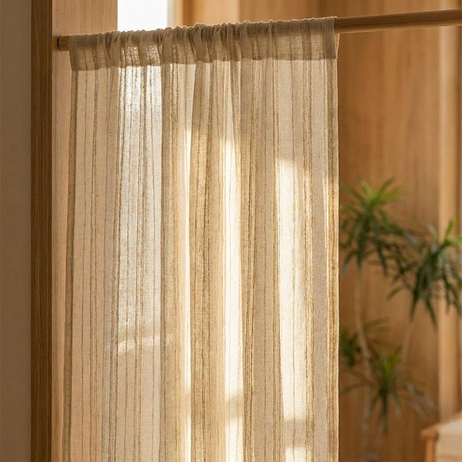 Gros plan sur un rideau en gaze rayé beige suspendu à une tringle en bois, lumière tamisée