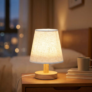 Lampe de chevet rétro allumée en lin blanc et bois avec lumière chaude tamisée sur une table de nuit