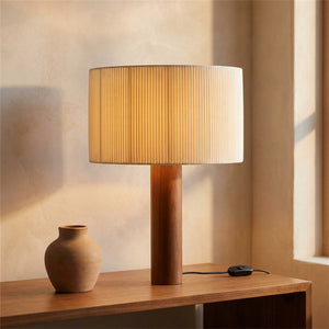 Lampe de table en bois massif avec abat-jour plissé beige allumée sur une console dans un intérieur chaleureux