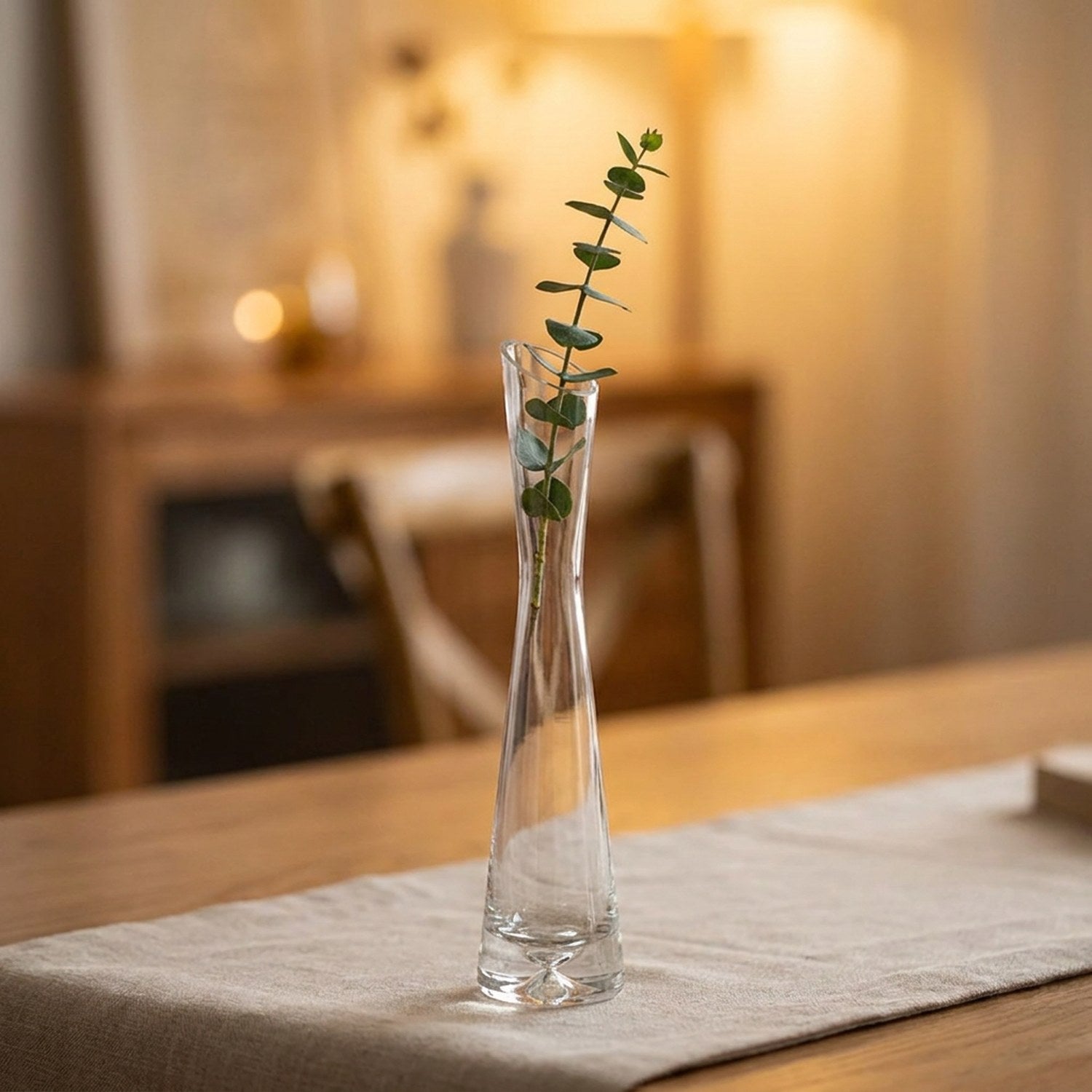 Vase soliflore en verre transparent à bouche inclinée avec une tige d'eucalyptus sur une table en bois