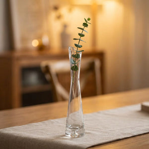 Vase soliflore en verre transparent à bouche inclinée avec une tige d'eucalyptus sur une table en bois