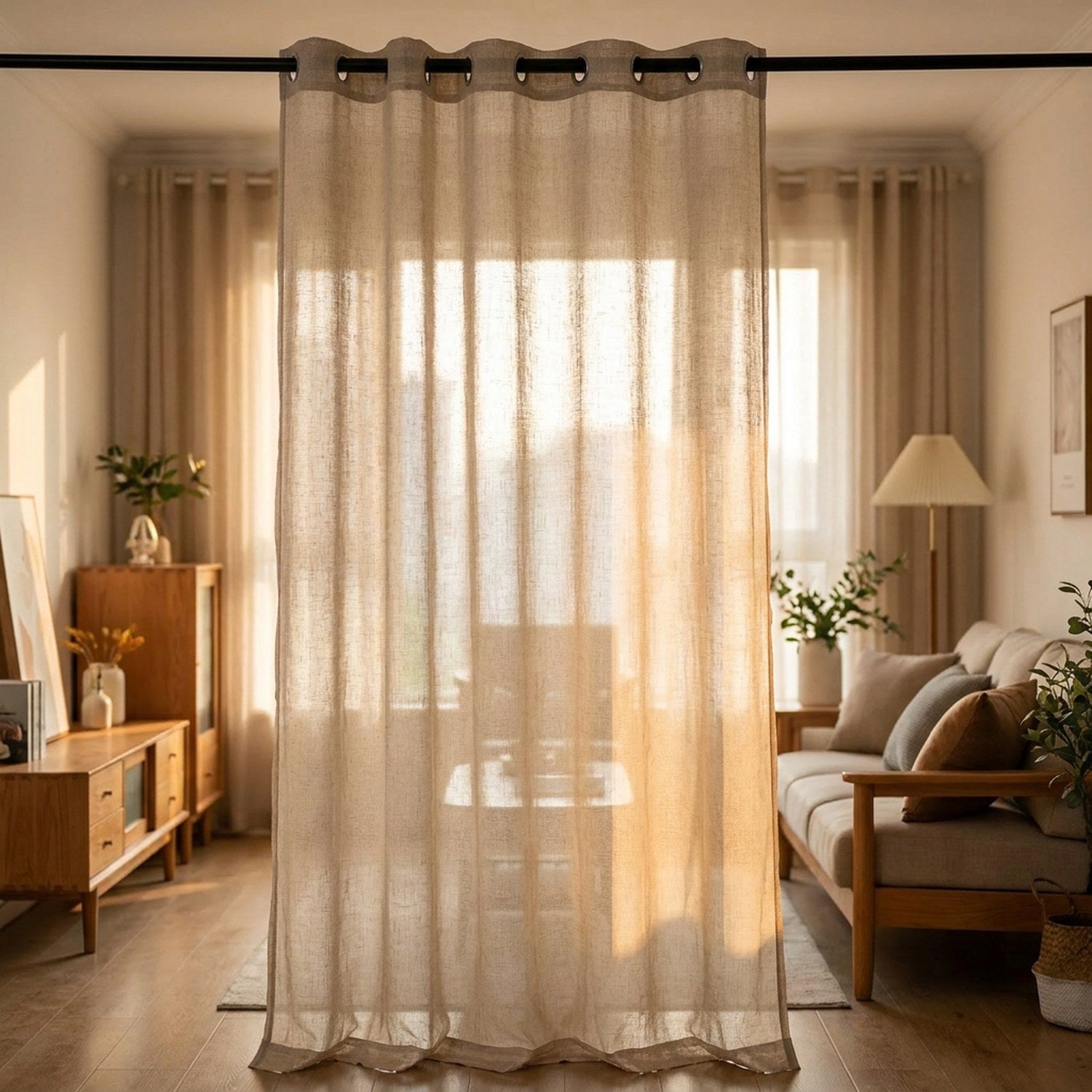 Voilage en tulle beige translucide suspendu à une fenêtre de salon baignée de lumière douce