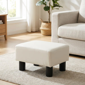 Tabouret repose-pieds blanc en similicuir posé sur un tapis clair devant un canapé dans un salon lumineux