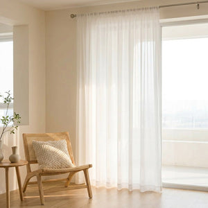 Voilage en tulle blanc dans un salon lumineux avec fauteuil en rotin