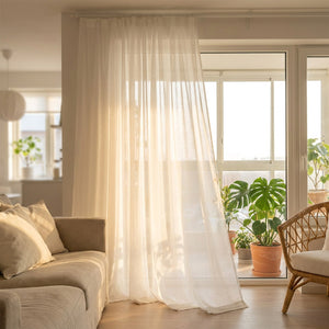 Voilage blanc du sol au plafond devant une baie vitrée de salon avec canapé et plantes vertes