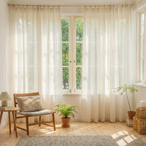 Rideau voilage effet lin dans un salon lumineux avec fauteuil bois et plante