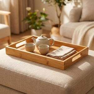 Plateau en bambou avec une théière et deux tasses sur un repose-pieds en lin dans un salon
