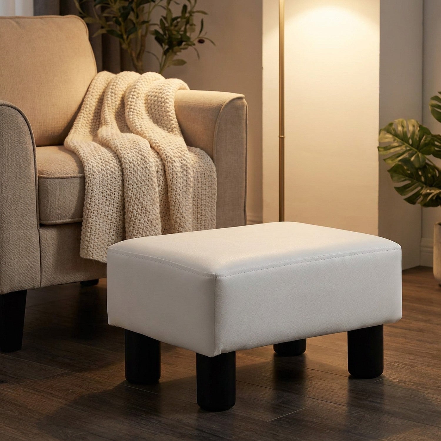 Tabouret repose-pieds blanc à côté d'un fauteuil beige avec un plaid tricoté dans un coin lecture chaleureux