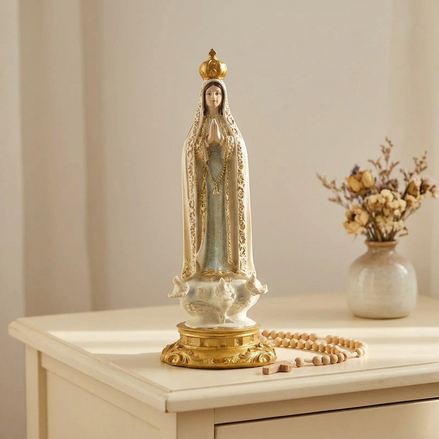 Figurine de Notre-Dame de Fatima sur une commode crème avec un chapelet et des fleurs séchées