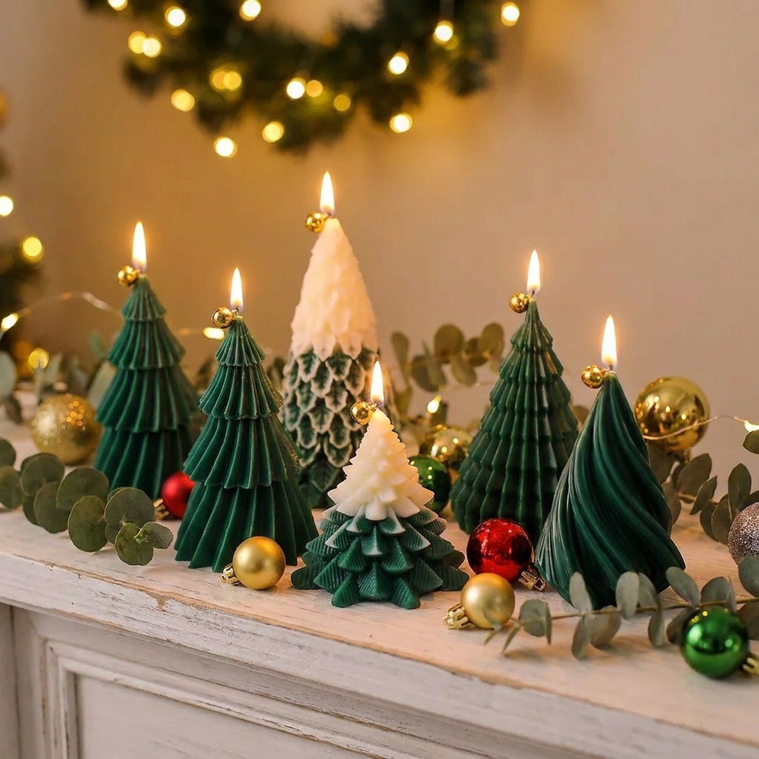 Bougies sapin de Noël allumées sur une cheminée avec eucalyptus et boules dorées