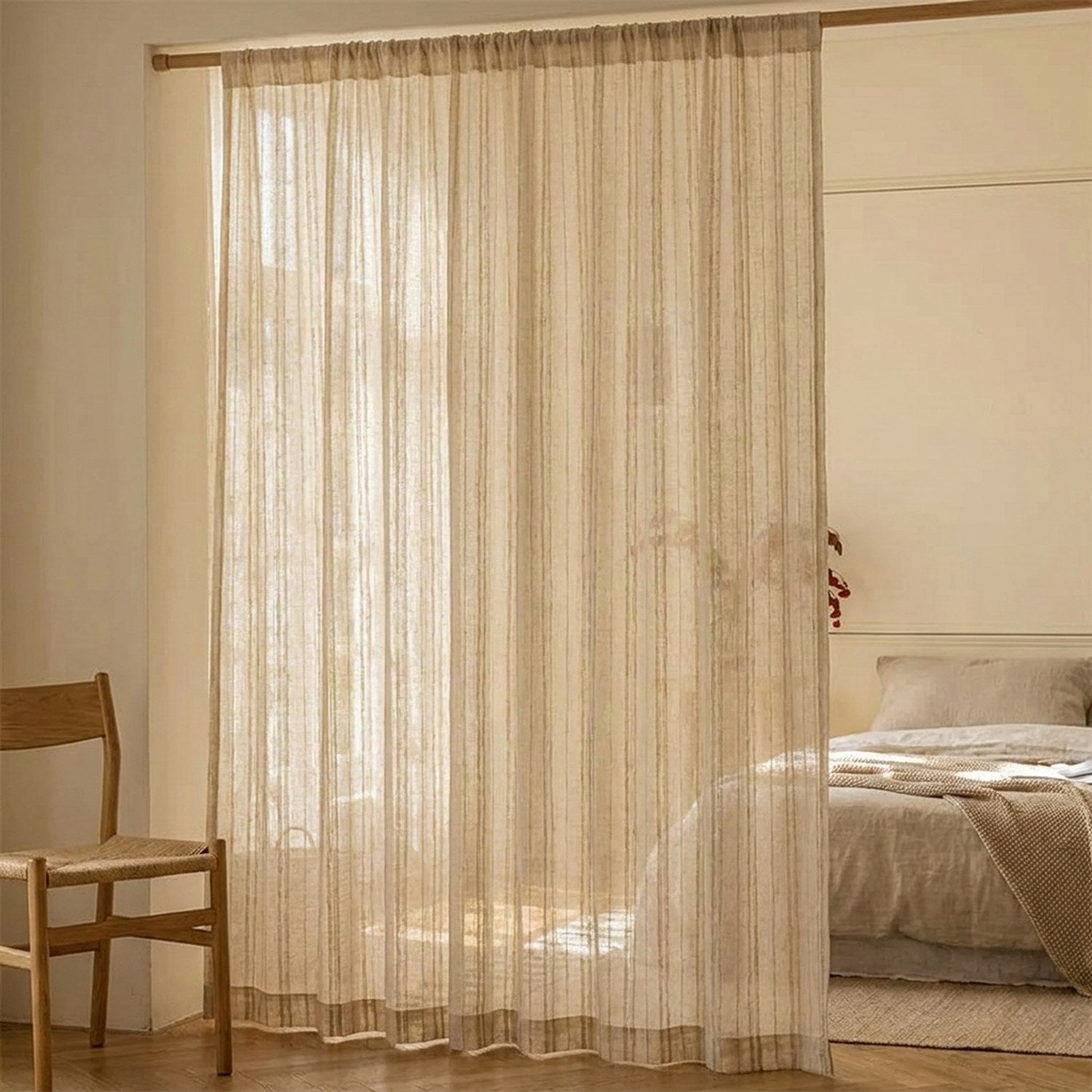 Rideau en gaze rayé suspendu devant une fenêtre de chambre avec chaise en bois